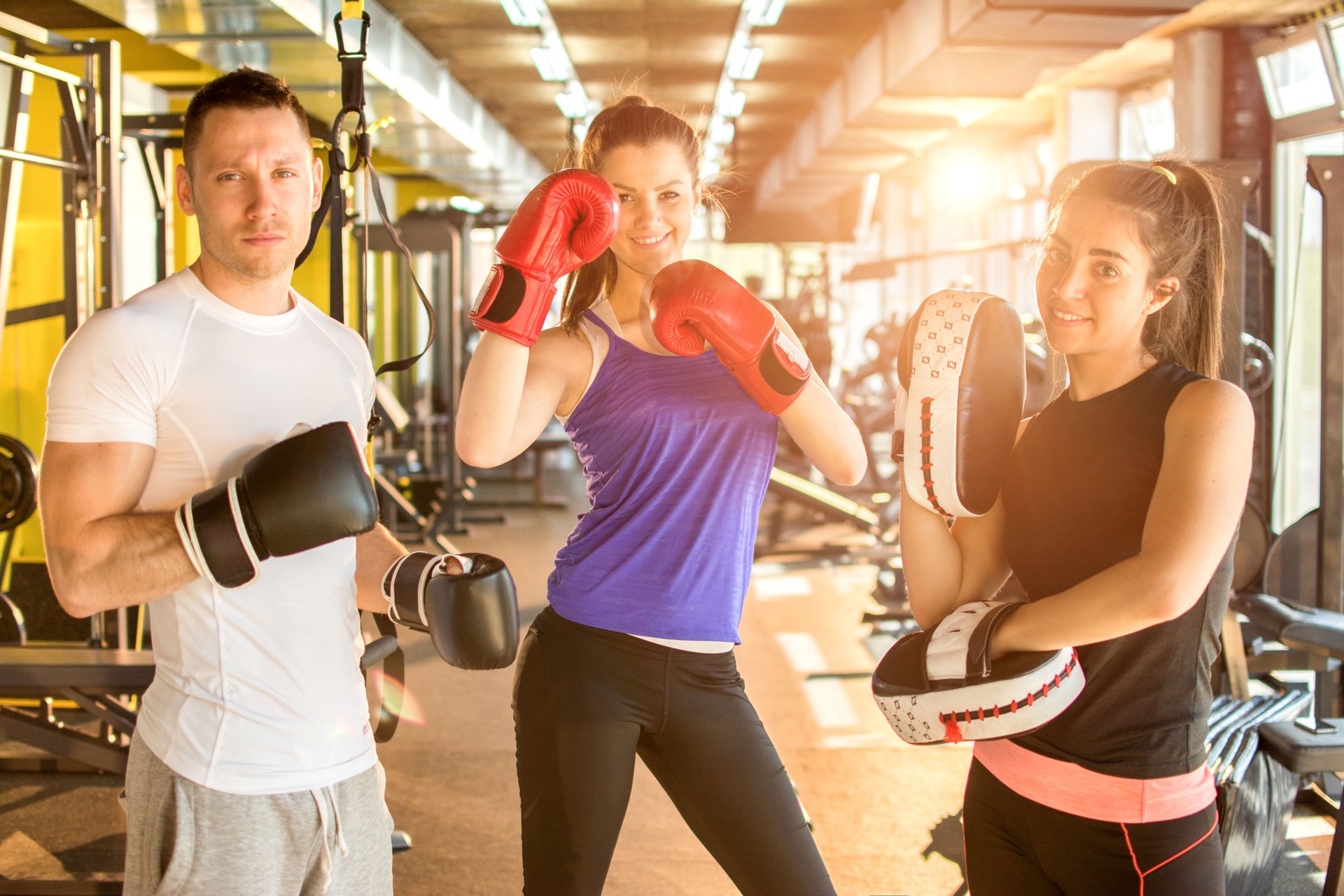 Group of three young people with boxing gloves posing together in gym.